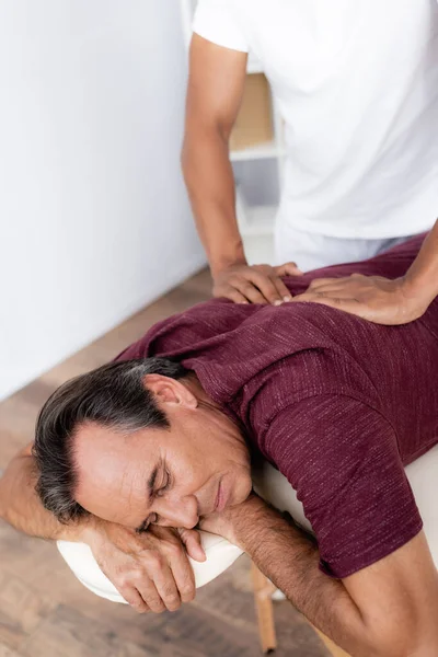 Joven africano americano masajista masaje espalda de mediana edad hombre en masaje mesa - foto de stock