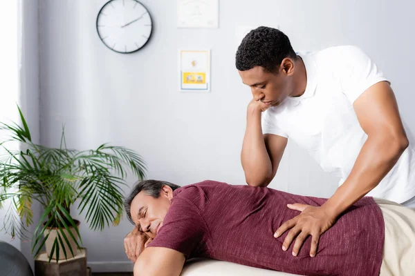 Afro-americano fisioterapeuta massageando de volta de homem de meia-idade na mesa de massagem — Fotografia de Stock