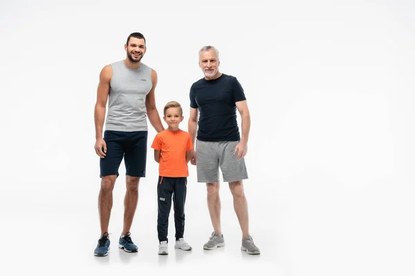Ragazzo felice con papà e nonno in abbigliamento sportivo guardando la fotocamera su bianco — Foto stock