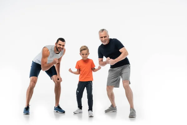 Boy with dad and grandfather in sportswear demonstrating strength while smiling at camera on white — Stock Photo