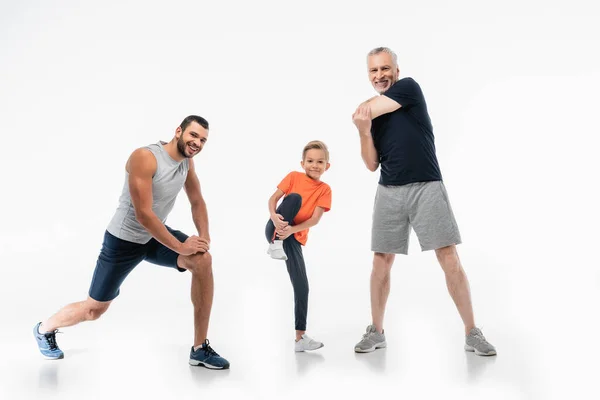 Garçon avec papa et grand-père en vêtements de sport démontrant la puissance tout en souriant à la caméra sur blanc — Photo de stock