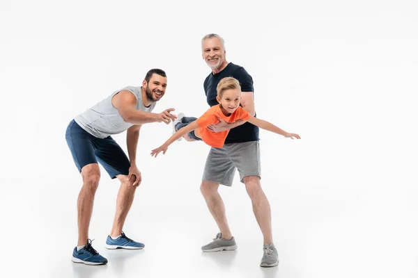 Feliz abuelo sosteniendo niño imitando vuelo cerca hombre apuntando con el dedo en blanco - foto de stock