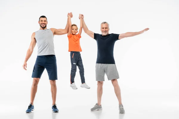 Allegro padre e nonno in abbigliamento sportivo tenendo ragazzo e sorridendo alla macchina fotografica su bianco — Foto stock