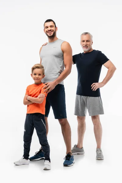 Ragazzo felice in piedi con le braccia incrociate vicino a papà e nonno in abbigliamento sportivo su bianco — Foto stock