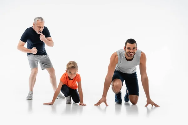 Mature man whistling near father and son in low start position on white — Stock Photo