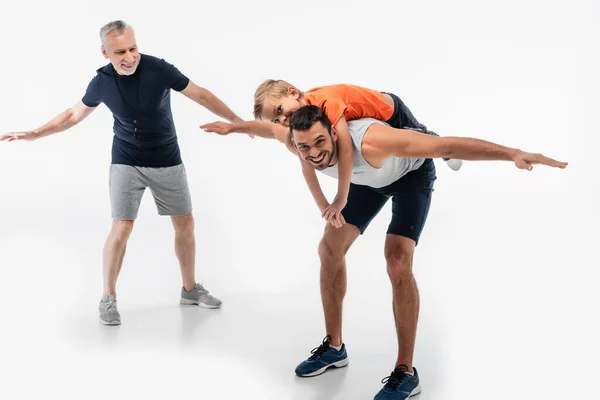 Glücklicher Vater huckepack Sohn in der Nähe Opa imitiert Flugzeug auf weiß — Stockfoto