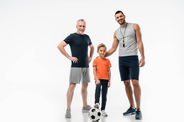 Happy father and grandpa near smiling boy stepping on soccer ball on white — Stock Photo