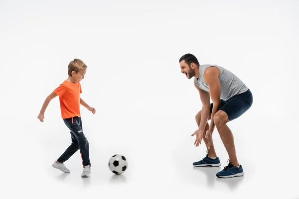 Взволнованные отец и сын в спортивной одежде играть в футбол на белом — стоковое фото