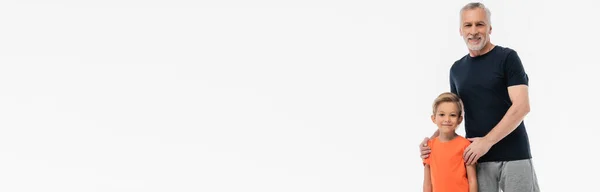Счастливый человек в спортивной одежде обнимает плечи внука, улыбаясь в камеру, изолированную на белом, баннер — стоковое фото