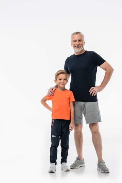 Lächelnder Großvater und glücklicher Enkel in Sportbekleidung, der in die Kamera auf Weiß blickt — Stockfoto