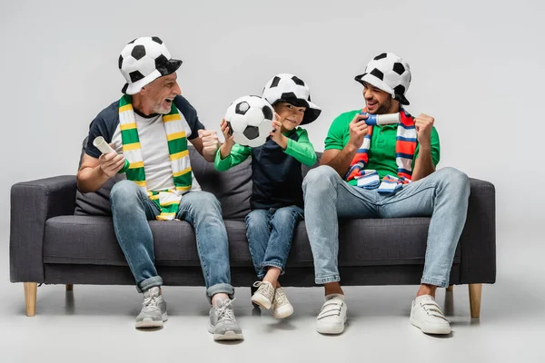 Homme heureux montrant geste de victoire tout en regardant match de football avec son fils et son petit-fils sur gris — Photo de stock