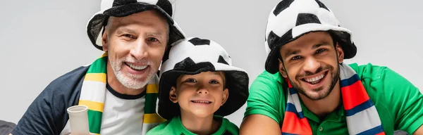Щасливий хлопчик з татом і дідусем у фан-капелюхах дивиться футбольний матч ізольовано на сірому, банер — стокове фото