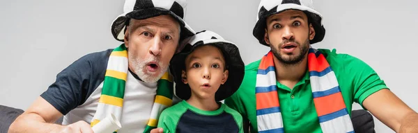Uomini stupiti e ragazzo in cappelli da tifoso a guardare la partita di calcio isolata sul grigio, striscione — Foto stock