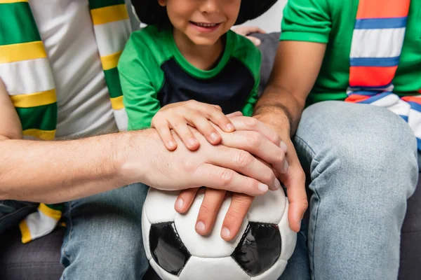 Cropped view of smiling boy, father and grandfather putting hands on soccer ball together — Stock Photo