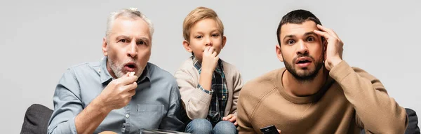 Hombres asombrados y niño viendo la televisión y comer palomitas de maíz aislado en gris, pancarta - foto de stock