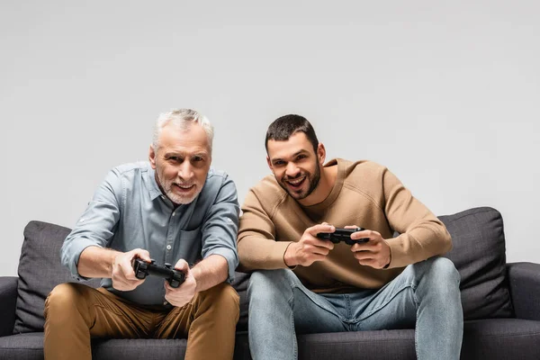 KYIV, UCRANIA - 17 de noviembre de 2020: padre e hijo alegres jugando videojuegos con joysticks aislados en gris - foto de stock