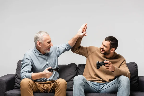 KYIV, UKRAINE - NOVEMBER 17, 2020: happy father and son giving high five while holding joysticks isolated on grey — Stock Photo