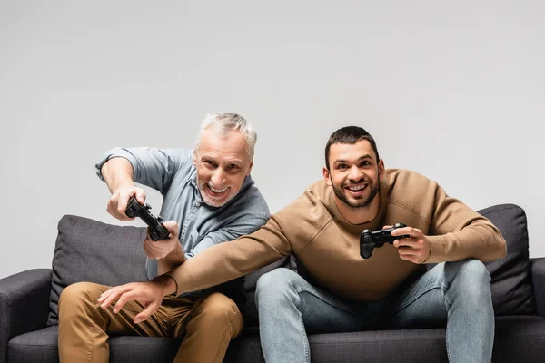 KYIV, UKRAINE - NOVEMBER 17, 2020: excited father and son playing video game on sofa isolated on grey — Stock Photo