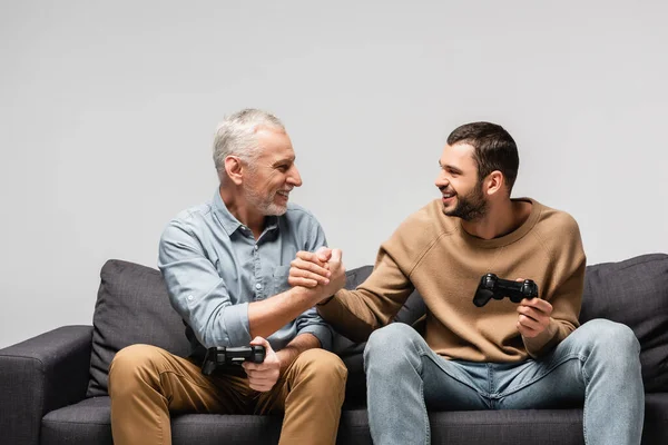 KIEW, UKRAINE - 17. NOVEMBER 2020: fröhlicher Vater und Sohn schütteln Hände, während sie Steuerknüppel isoliert auf grau halten — Stockfoto