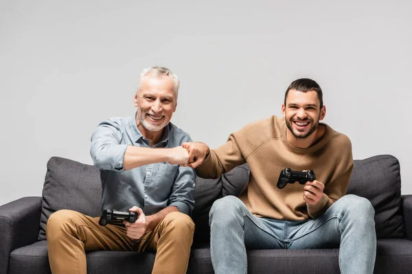 KYIV, UKRAINE - 17 NOVEMBRE 2020 : père et fils heureux faisant une première bosse tout en tenant des joysticks isolés sur du gris — Photo de stock