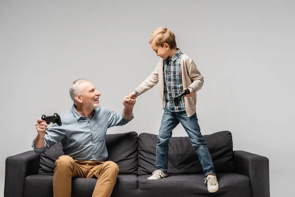 KYIV, UKRAINE - 17 NOVEMBRE 2020 : un homme heureux fait une première bosse avec son petit-fils tout en tenant un joystick isolé sur du gris — Photo de stock