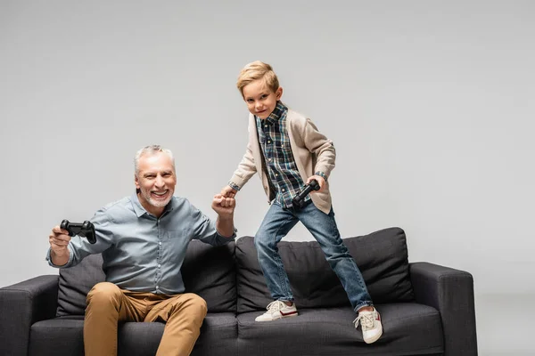 KYIV, UKRAINE - NOVEMBER 17, 2020: happy man with smiling grandson doing fist bump while holding joysticks isolated on grey — Stock Photo