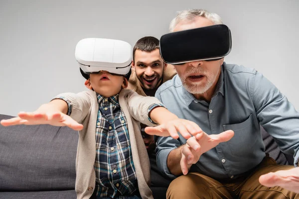 Grandfather and grandson gesturing in vr headsets near excited man on background isolated on grey — Stock Photo