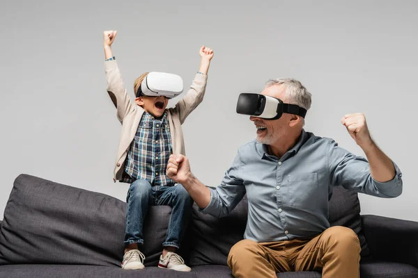 Excited man and boy in vr headsets showing win gesture isolated on grey — Stock Photo