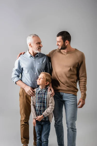 Glückliche Männer, die einander in der Nähe lächelnden Jungen isoliert auf grau anschauen — Stockfoto