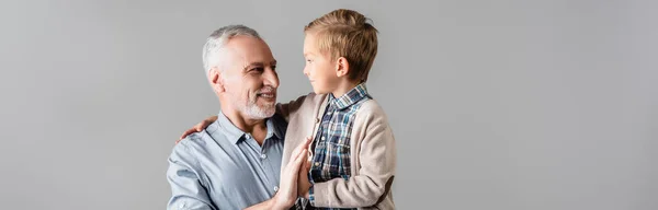 Feliz hombre dando alta cinco a nieto mientras lo mantiene aislado en gris, bandera - foto de stock