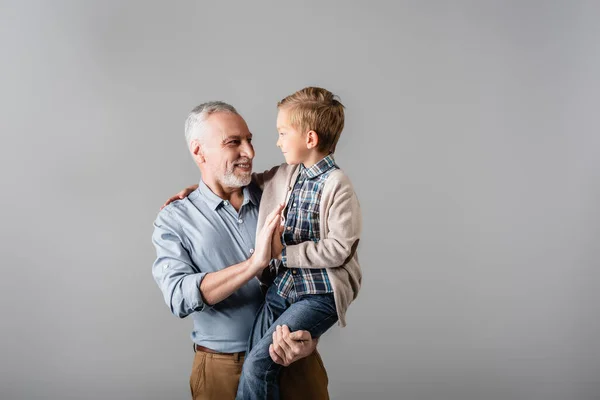 Felice nonno dare il cinque al nipote, mentre lo tiene isolato su grigio — Foto stock