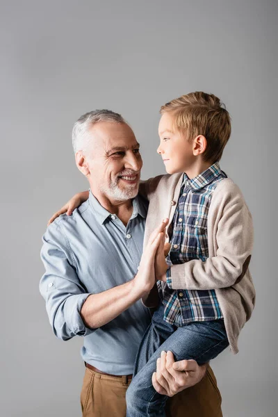 Sorridente nonno che dà il cinque al nipote mentre lo tiene isolato sul grigio — Foto stock