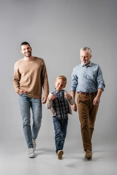 Hombres alegres y niño sonriente en ropa casual caminando sobre gris - foto de stock