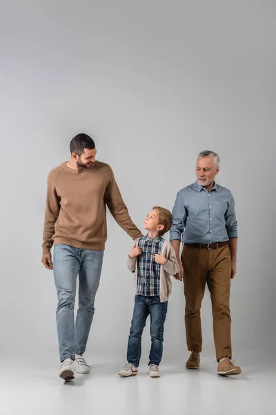 Glücklicher Junge schaut Vater beim Gehen in der Nähe von Opa auf grau — Stockfoto