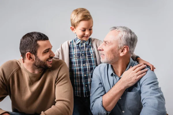 Feliz niño abrazando papá y abuelo aislado en gris - foto de stock