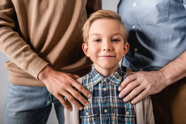 Hommes touchant épaules de garçon heureux regardant caméra isolé sur gris — Photo de stock