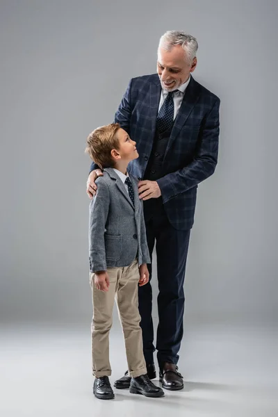 Улыбающийся бизнесмен в формальной одежде обнимает внука на серых плечах — стоковое фото