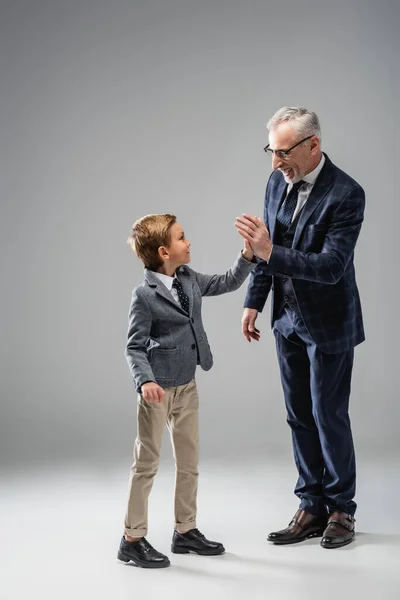 Happy mature businessman giving high five to grandson on grey — Stock Photo
