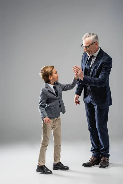 Heureux homme d'affaires mature donnant haute cinq à petit-fils sur gris — Photo de stock