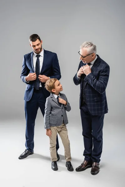 Homme d'affaires souriant regardant grand-père et petit-fils toucher des liens sur gris — Photo de stock