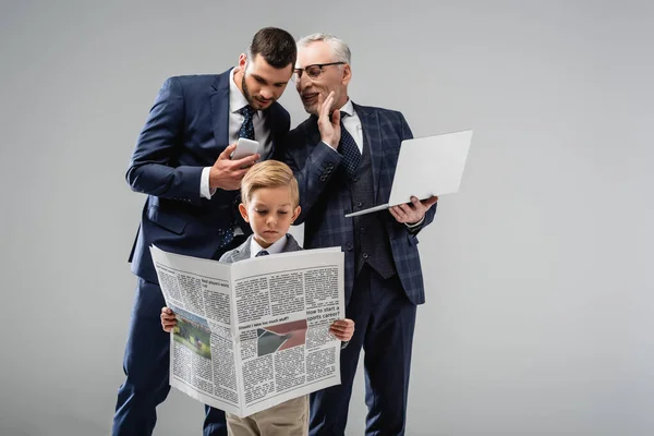 Homem de negócios maduro falando com filho perto menino em desgaste formal ler jornal isolado em cinza — Fotografia de Stock