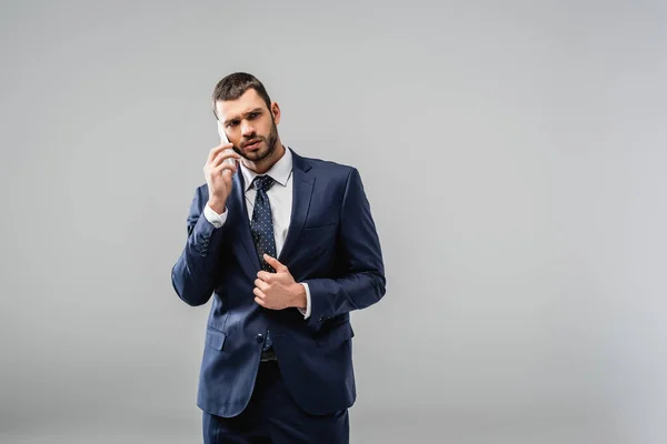 Uomo d'affari premuroso in giacca e cravatta che parla sul cellulare isolato su grigio — Foto stock