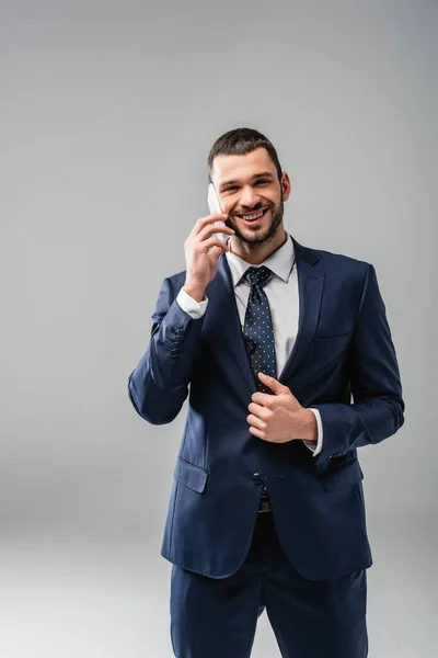 Hombre de negocios feliz en ropa formal hablando en el teléfono inteligente aislado en gris - foto de stock