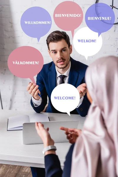 Interpreter talking to arabian business partner on blurred foreground, speech bubbles with welcome word in different languages illustration — Stock Photo