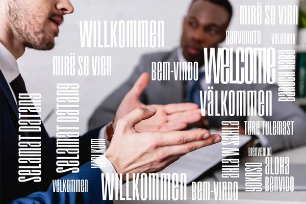 Interpreter gesturing near african american business partner on blurred background, welcome word in different languages illustration — Stock Photo