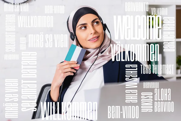 Intérprete árabe sonriente en auriculares con traductor digital en primer plano borroso, palabra de bienvenida en diferentes idiomas ilustración - foto de stock