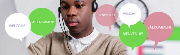 African american interpreter in headset near illustration of speech bubbles with word welcome in different languages, banner — Stock Photo