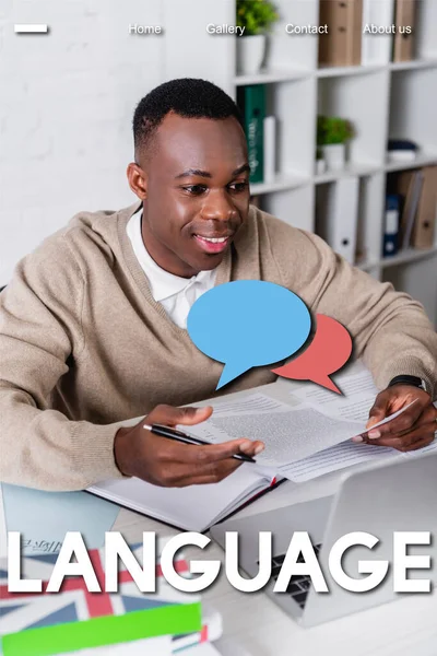 Sonriente intérprete afroamericano que trabaja en la computadora portátil en primer plano borroso, ilustración de burbujas de habla vacías cerca de la palabra de idioma - foto de stock