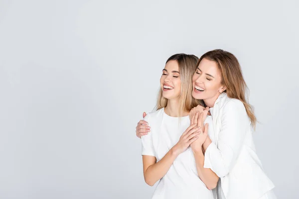 Feliz madre abrazando joven hija con los ojos cerrados aislados en gris - foto de stock