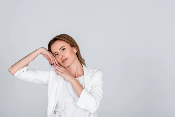 Femme en tenue blanche regardant la caméra tout en posant isolé sur gris — Photo de stock